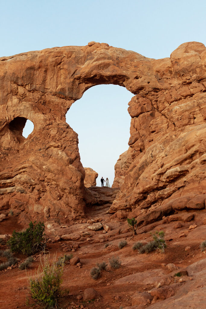 couple stands under double arches at Arches National Park Moab elopement