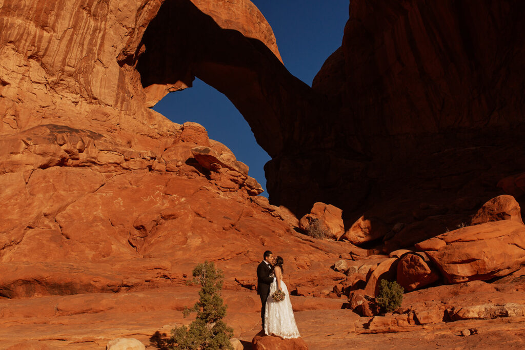 couple stands under arches at Arches National Park Moab elopement