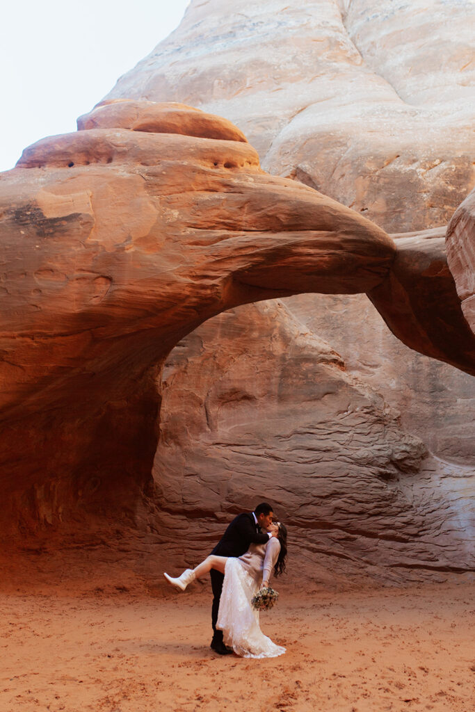 couple kisses in front of arches at Arches National Park Moab elopement
