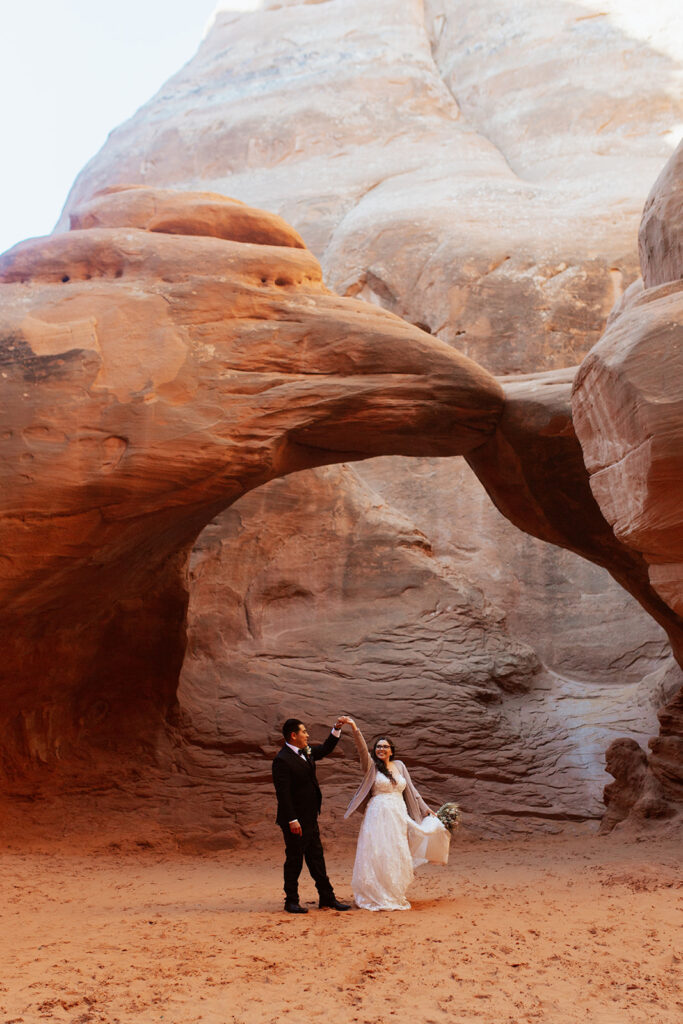 couple twirls under arches at Arches National Park Moab elopement