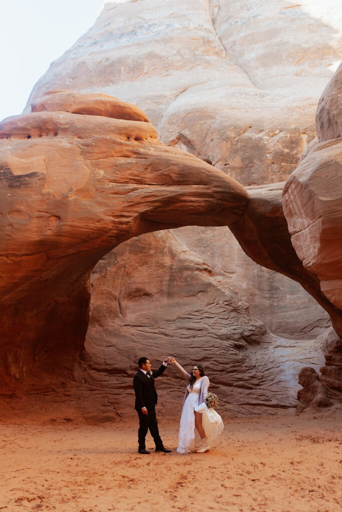 couple twirls under arches at Arches National Park Moab elopement