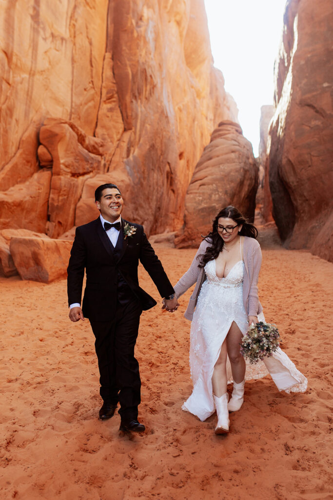 couple walks holding hands through Moab red rock elopement