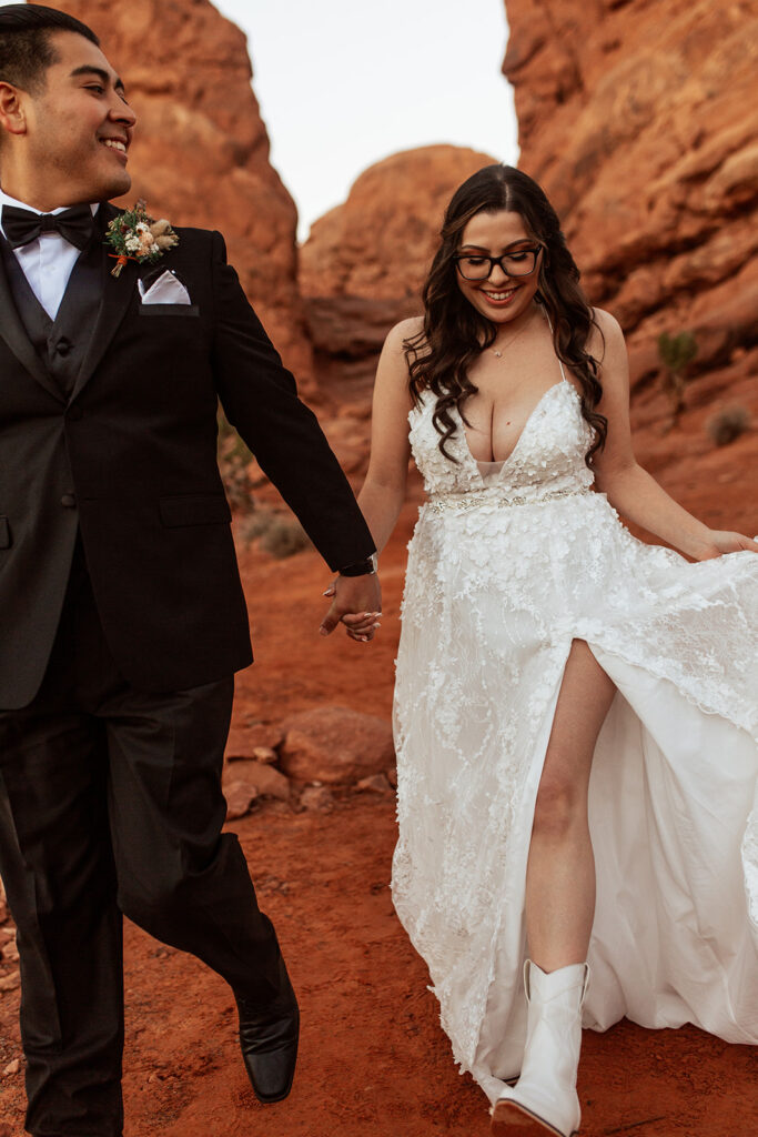 couple walks holding hands at red rock elopement