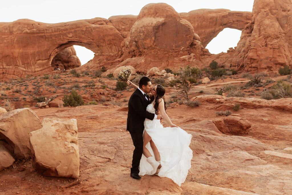 couple kisses under arches at red rock elopement
