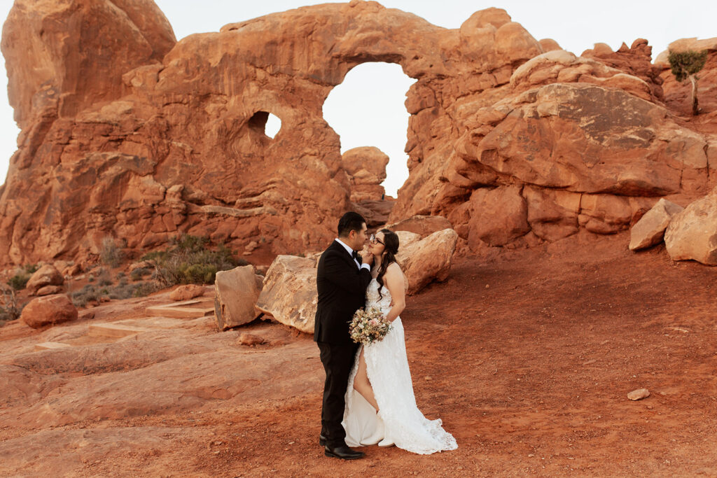 couple stands together in front of arches at Arches National Park Moab elopement