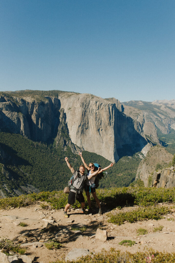 couple arms in the air over Yosemite Valley wearing backpacking gear
