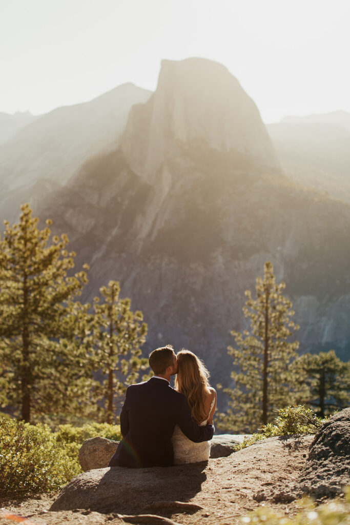 couple kisses seated in front of Half Dome at elopement