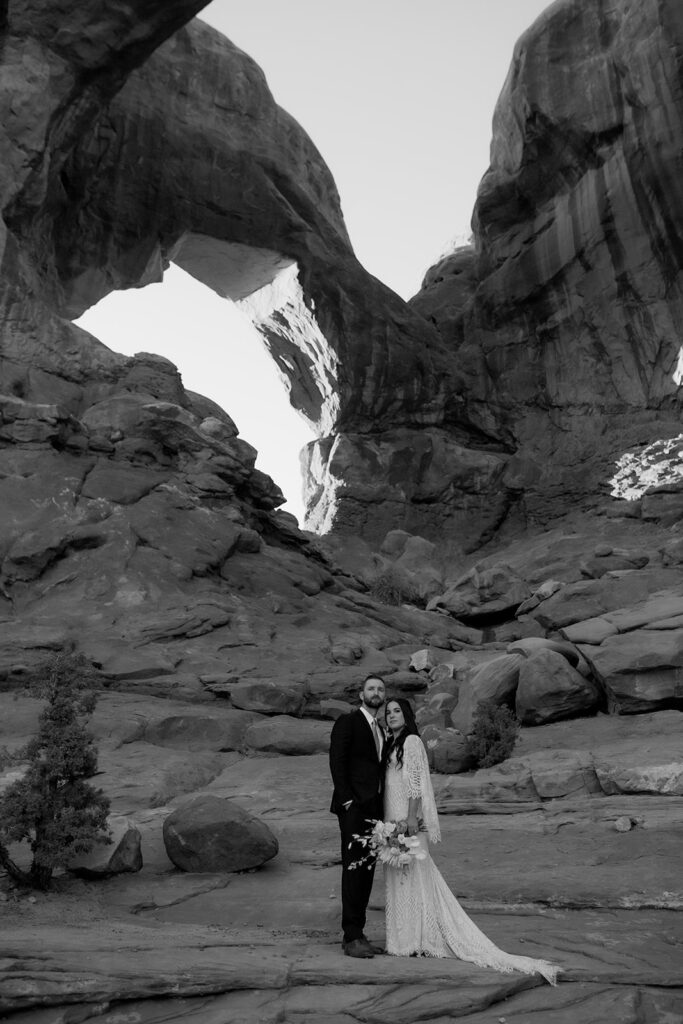 couple stands under arches at Arches National Park