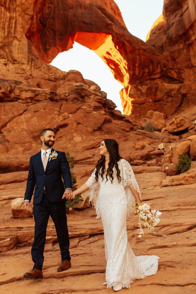 couple walks under arches at sunset Moab adventure elopement