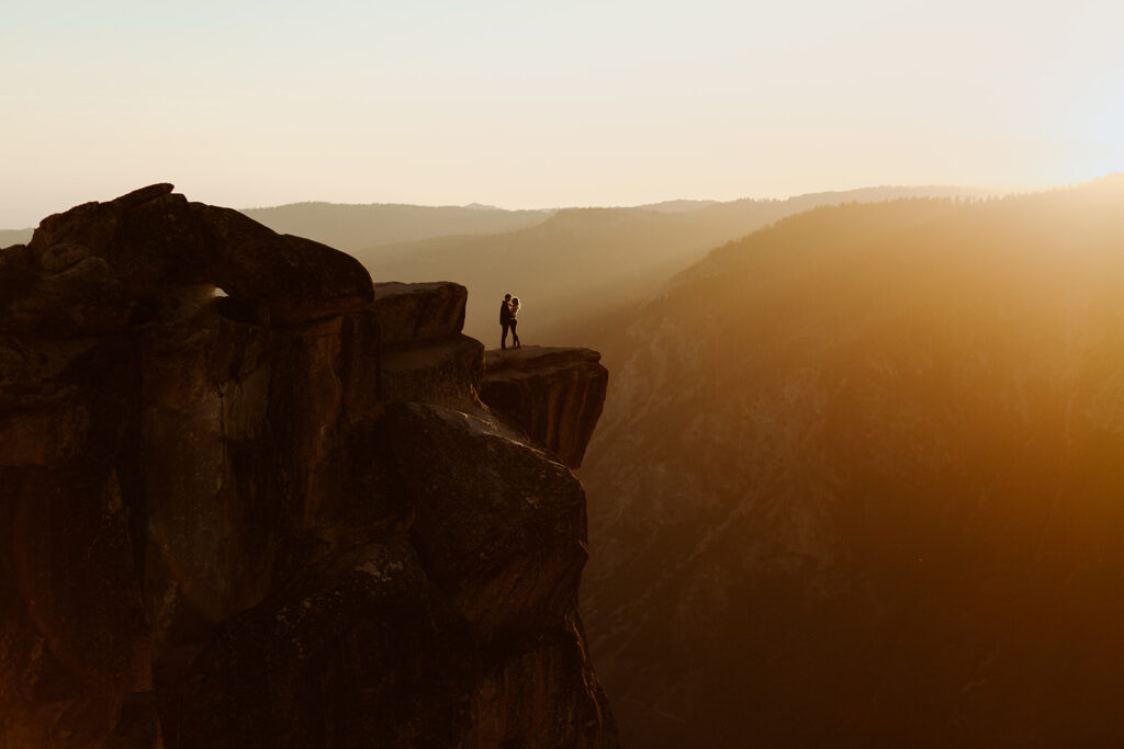 couple stands on cliff at sunset Taft Point engagement