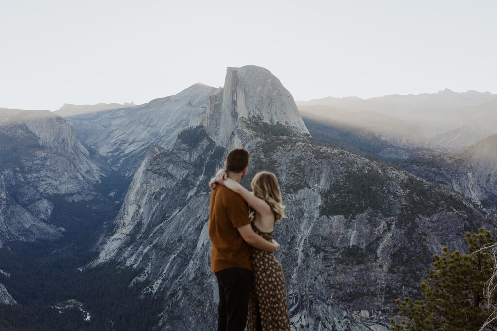 couple stands on Glacier Point overlook at Yosemite sunrise