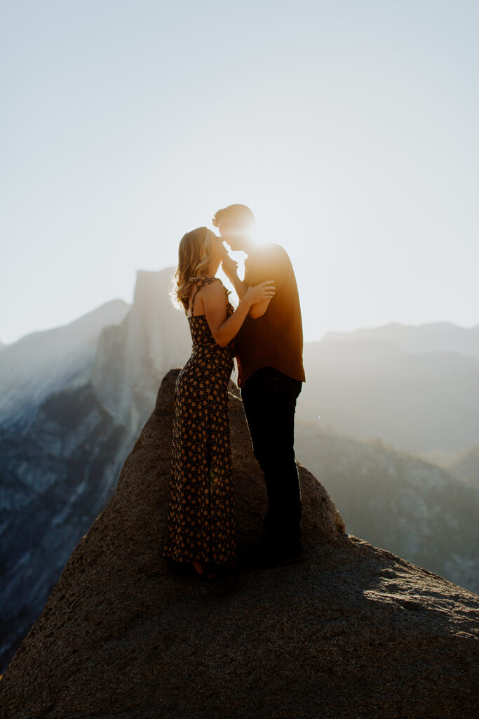 couple kisses on cliff at Glacier Point overlook engagement