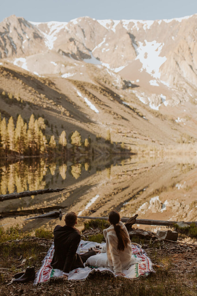 couple sits at lakeside picnic on mountain elopement