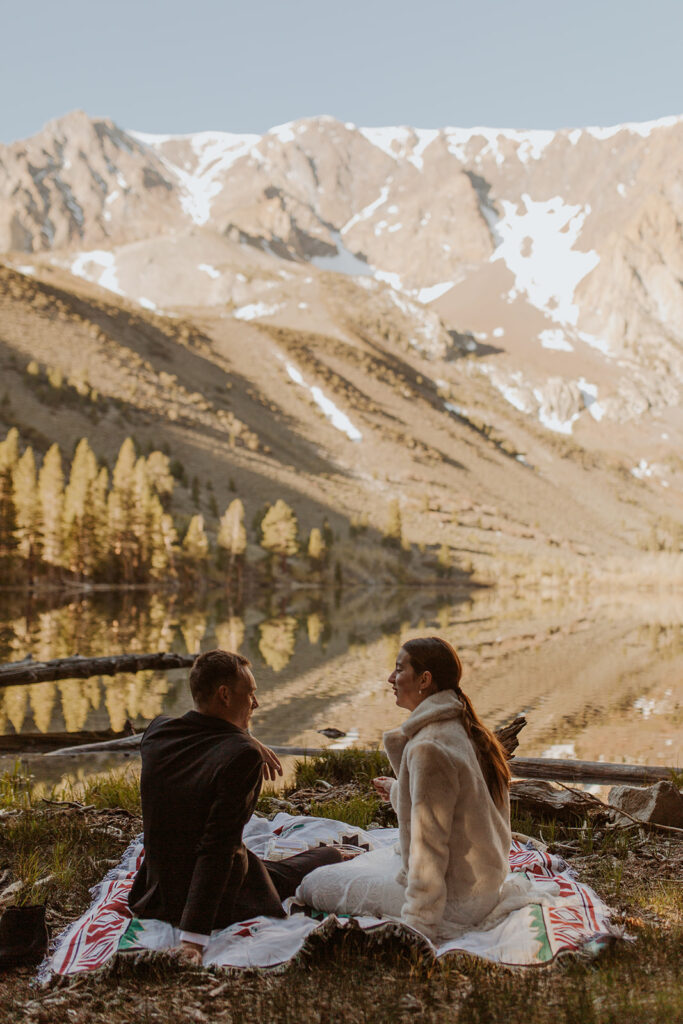 couple sits at lakeside picnic on mountain elopement