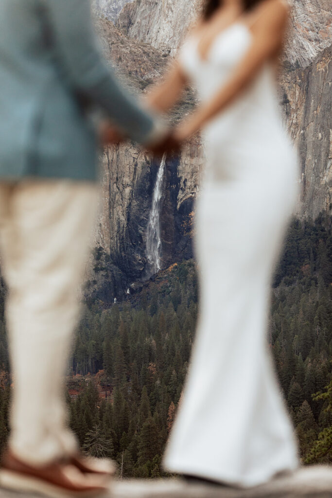 couple holds hands in front of Yosemite Falls