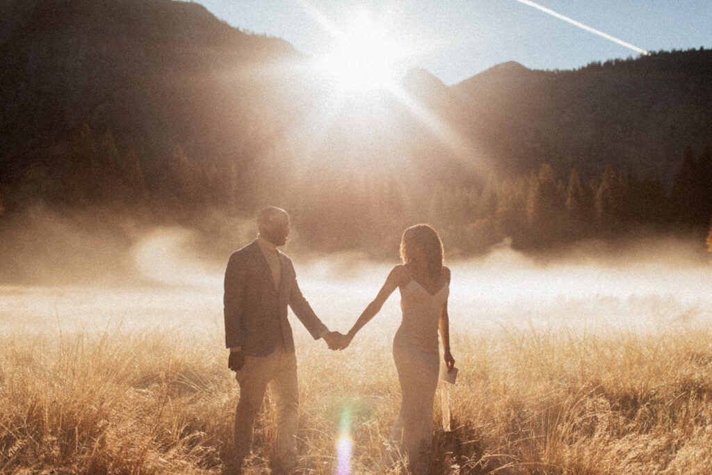 couple walks through sunny foggy field holding hands
