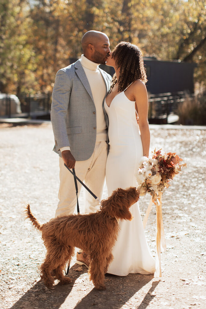 couple kisses while holding dog on leash at Yosemite elopement