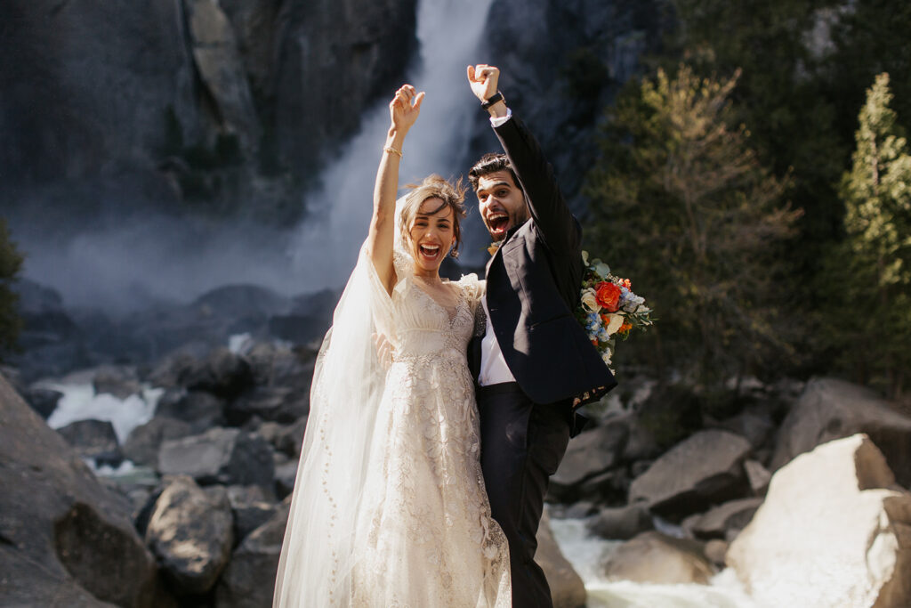 couple cheers beside Yosemite Falls at elopement
