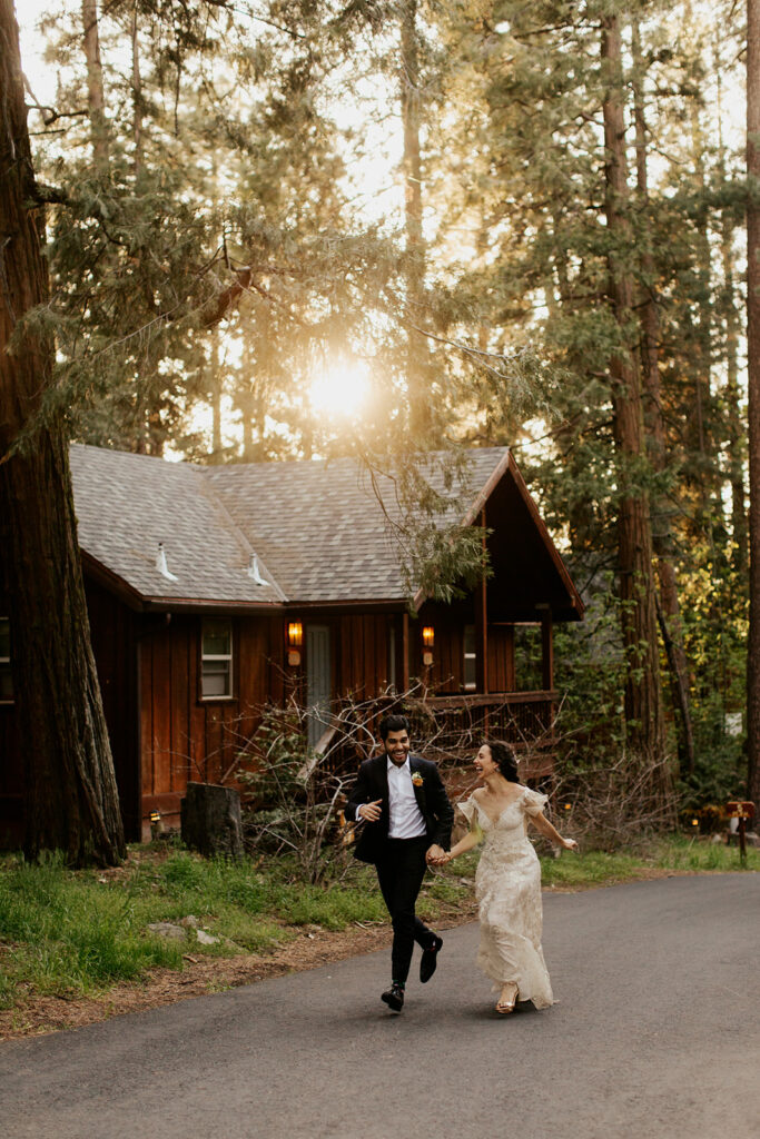 couple runs beside cabin in woods at sunset wedding