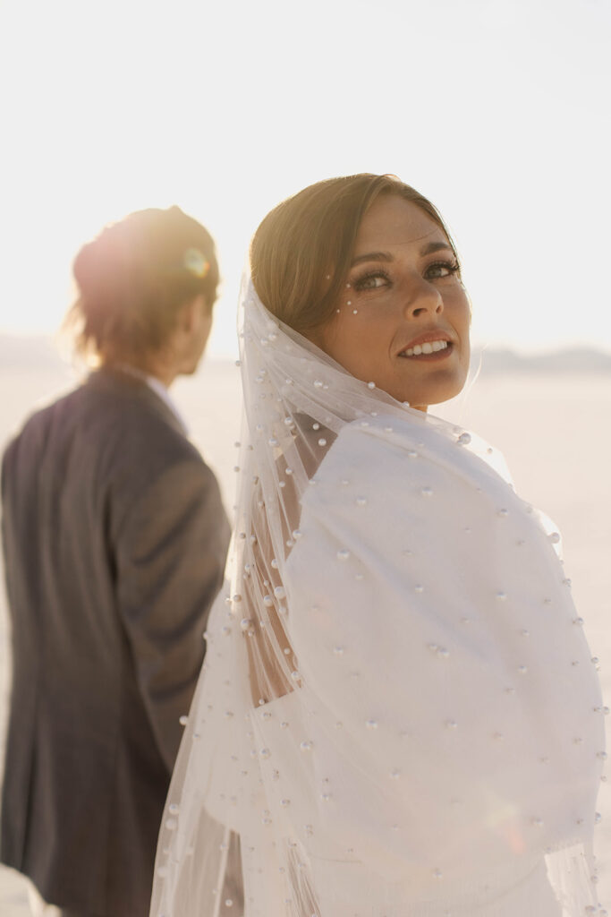 bride looks back wearing pearl-studded veil at Bonneville Salt Flats sunset elopement